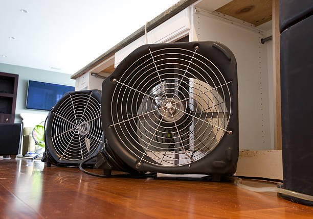 Two industrial fans running to dry out water damaged residential kitchen island from leak.