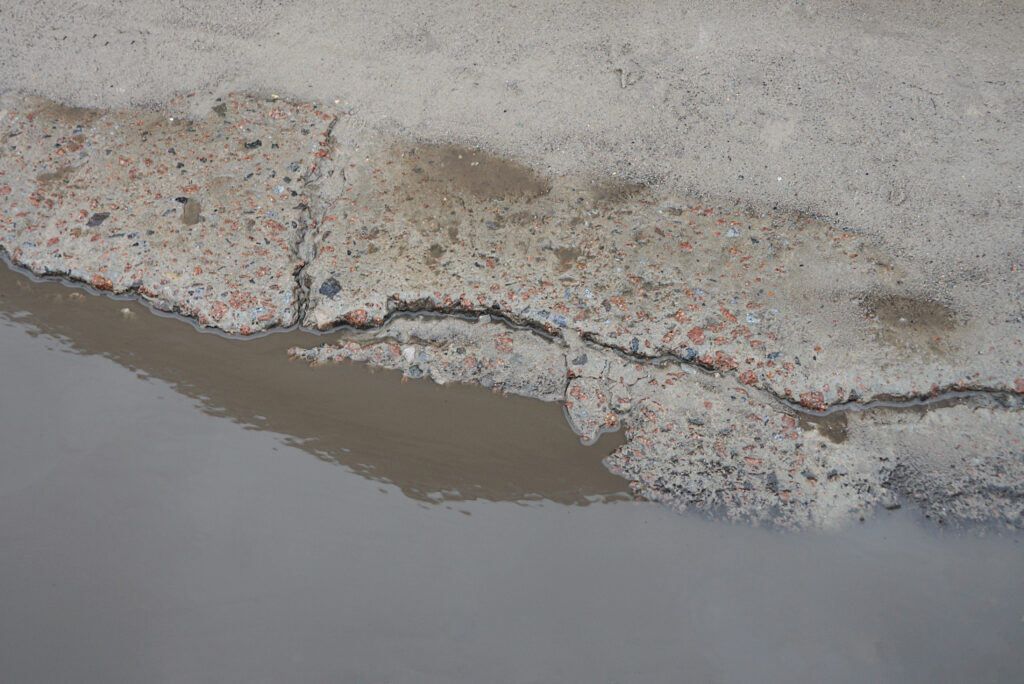part of a puddle with brown dirty water on a gray concrete pavement with cracks in the street